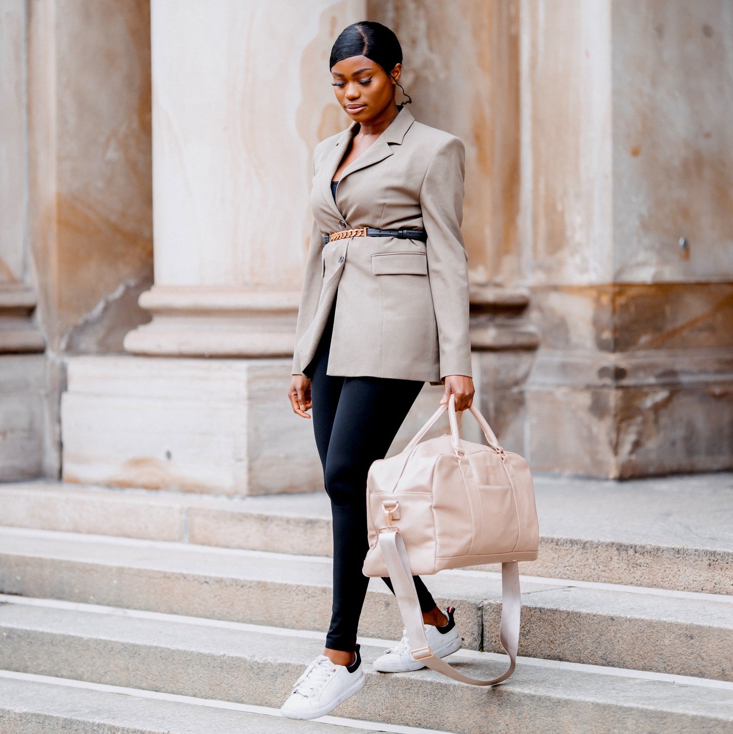 Eine Frau mit einer beigen Anzugjacke läuft Treppen runter und trägt dabei den Weekender LINUS in der Hand.
