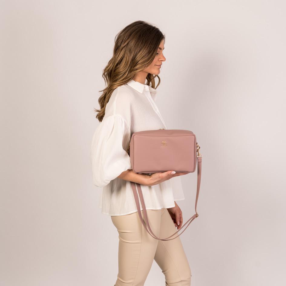Ein Model trägt die ZOE XL Crossbody in der Farbe Puder in der Hand und läßt den Gurt hängen