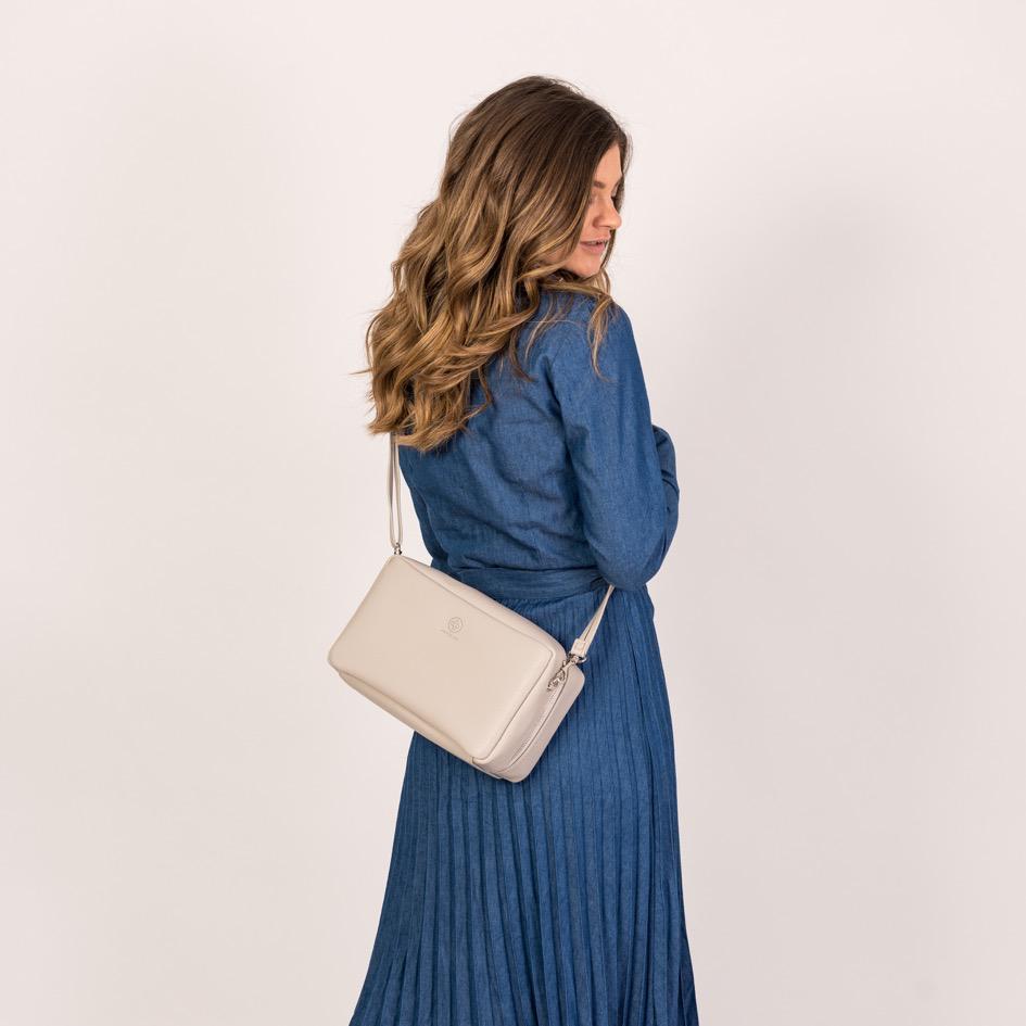Eine junge Frau schaut über die Schulter nach vorne und trägt die Crossbody ZOE XL in stone auf dem Rücken
