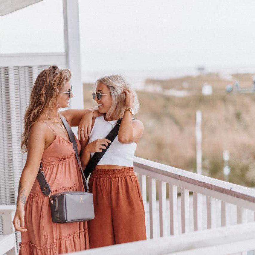 Zwei junge Frauen haben Spaß und tragen ihre Taschen crossbody