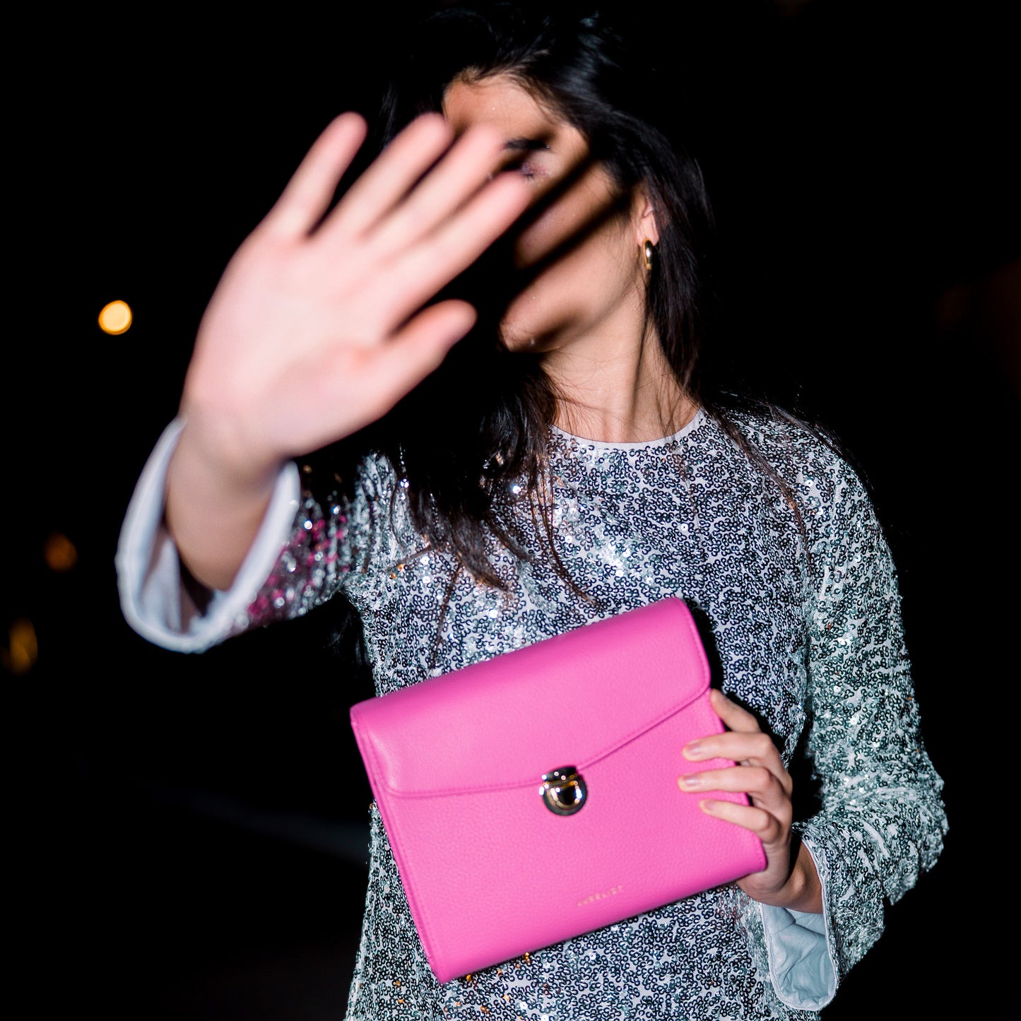 Das Model in einem Gliterkleid nutzt die Tasche um sich vor der Kamera abzuschotten.