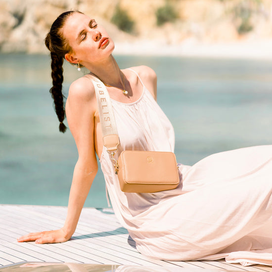 Frau sitzt mit einem simplen weißen Kleid vorm Hintergrund mit Meer, sie trägt den Signatur Strap an der Jade