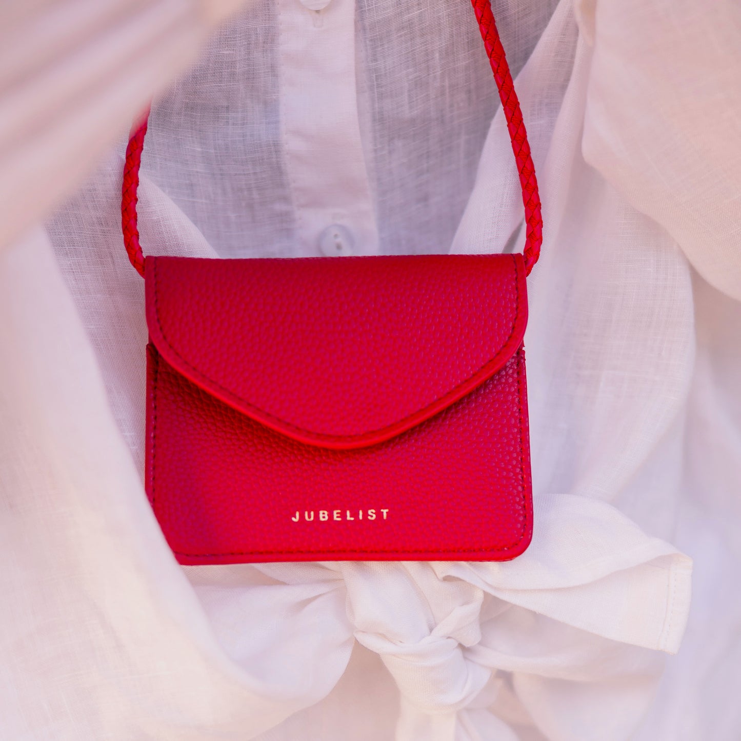 In Nahaufnahme wird das rote Portemonnaie BAILY gezeigt, im Hintergrund das weiße Leinenhemd.