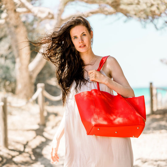 Das Model trägt den roten Shopper VICTORIA vor strahligem Hintergrund. Sie trägt ein schlichtes Beiges Kleid.