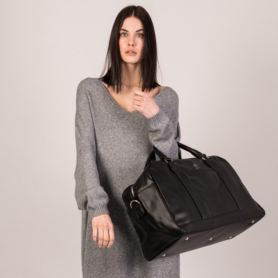 Eine junge Frau trägt den Weekender in schwarz an den Griffen über ihre Armbeuge