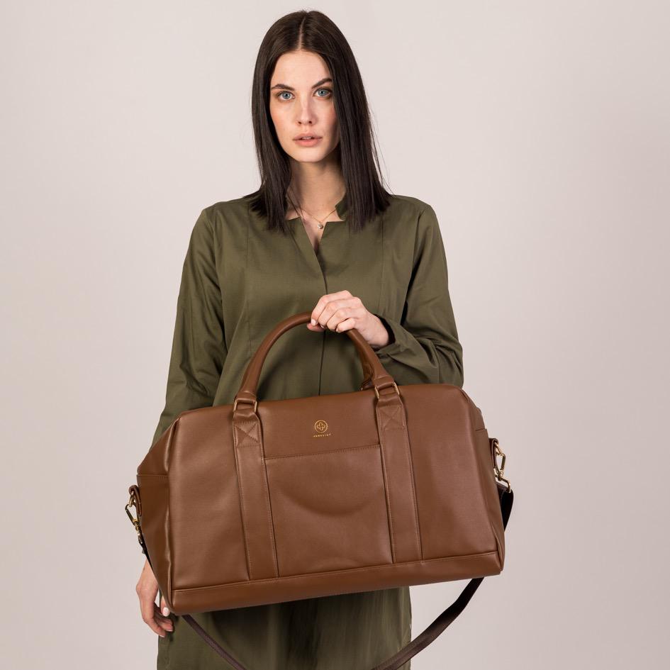 Der Linus in coffee wird an seinen Griffen in die Höhe gehalten und der dazu gehörende Schultergurt baumelt runter