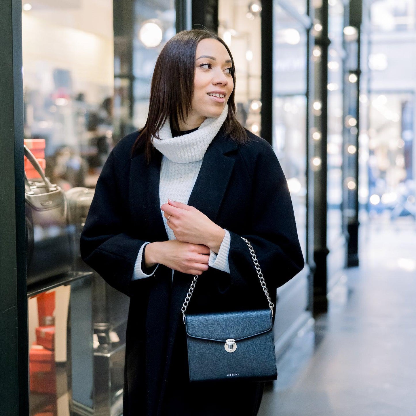 Eine junge Frau trägt ihre Tasche in schwarz  silber an der dicken Kette über ihren Unterarm