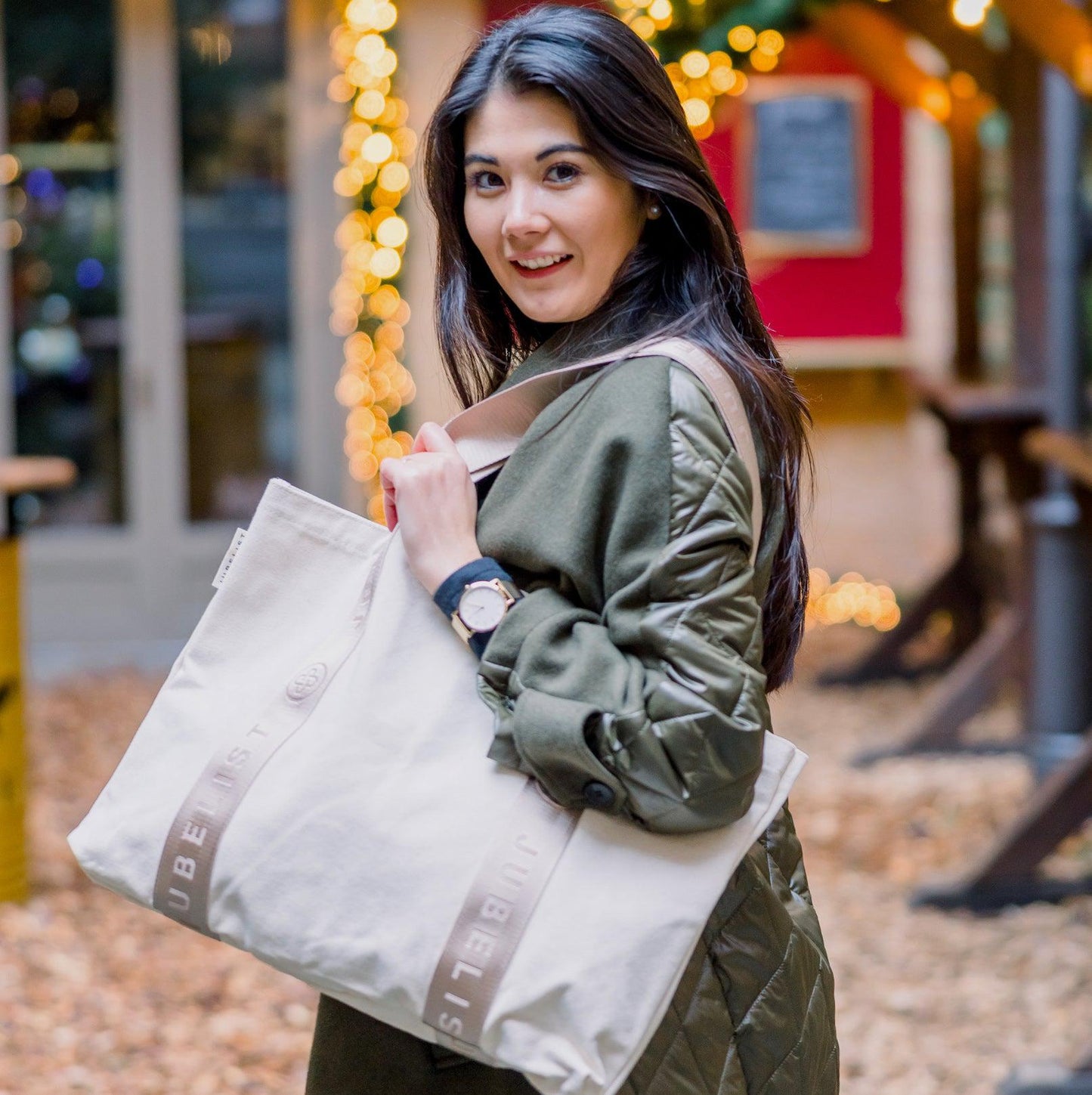 Eine junge Frau trägt den Canvas Shopper in sand über der Schulter und lächelt in die Kamera