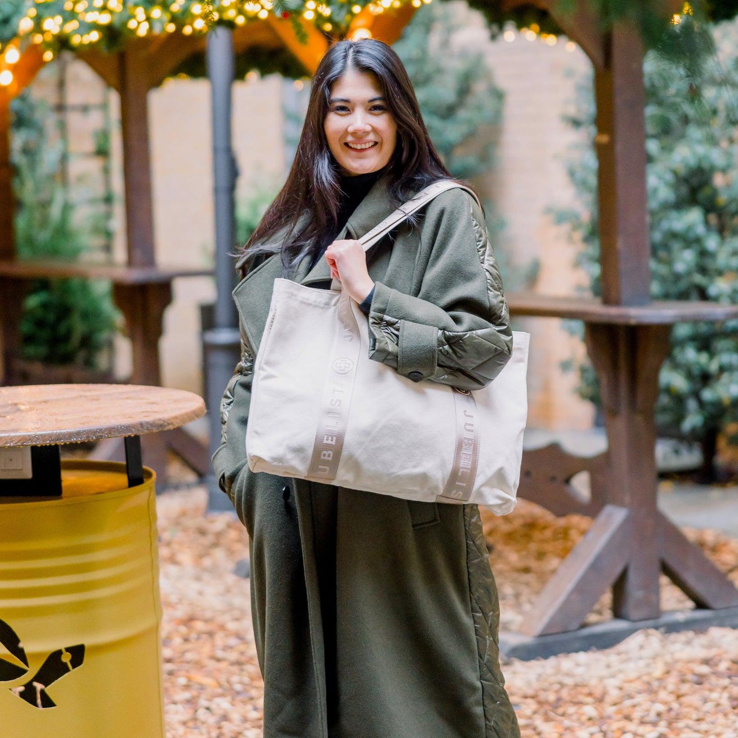 Eine junge Frau trägt den Canvas Shopper in sand über der Schulter und hält sich am Tragegurt fest