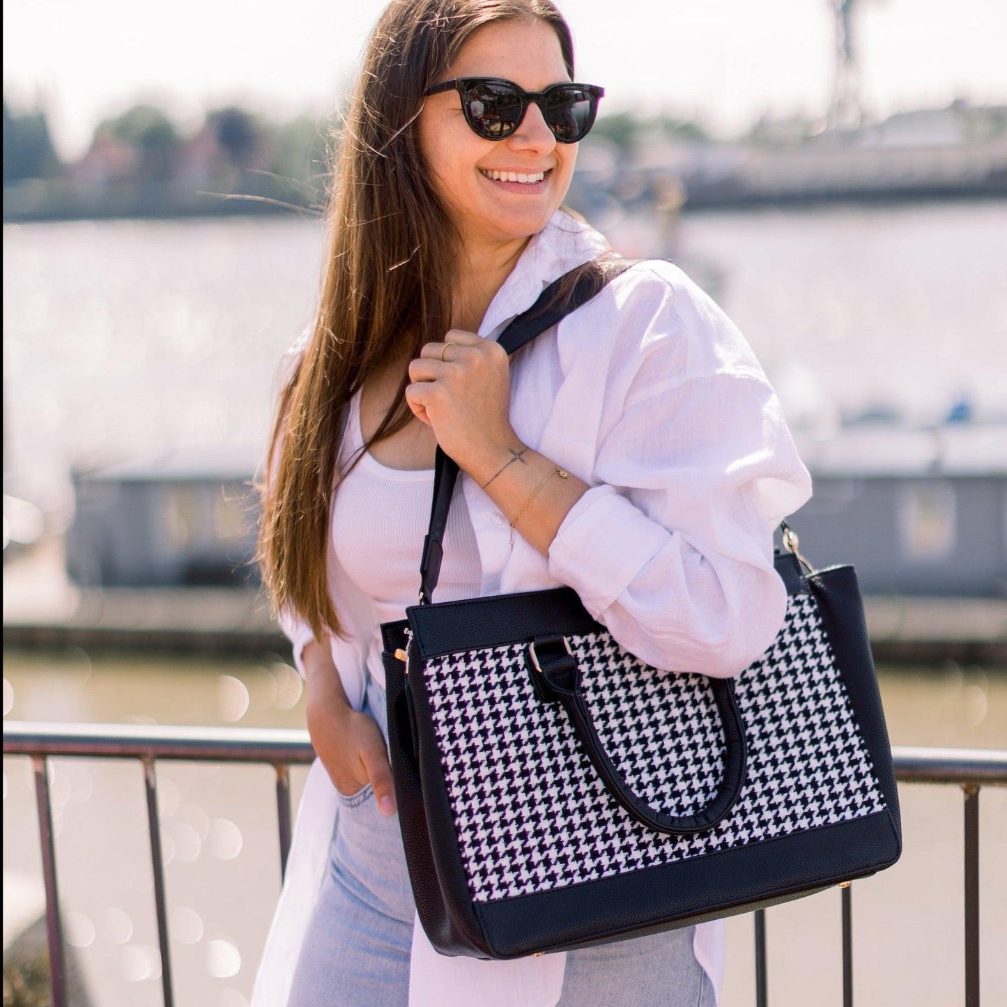 Ein strahlendes Model mit Sonnenbrille trägt die Business Bag in black and white zu einer weißen Bluse mit einer hellblauen Jeans