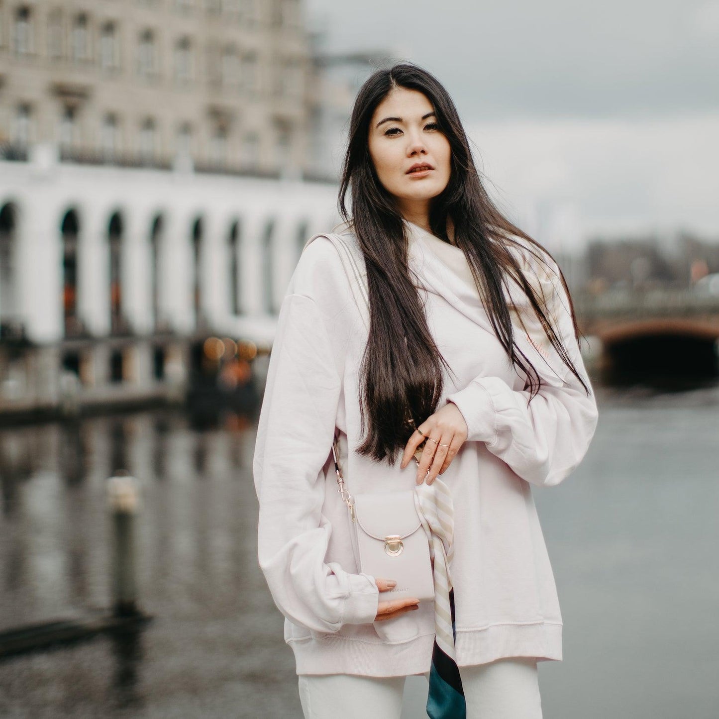 Eine junge Frau trägt die Tasche in Flieder mit einem Universal Strap iin beige-weiß über ihre Schulter