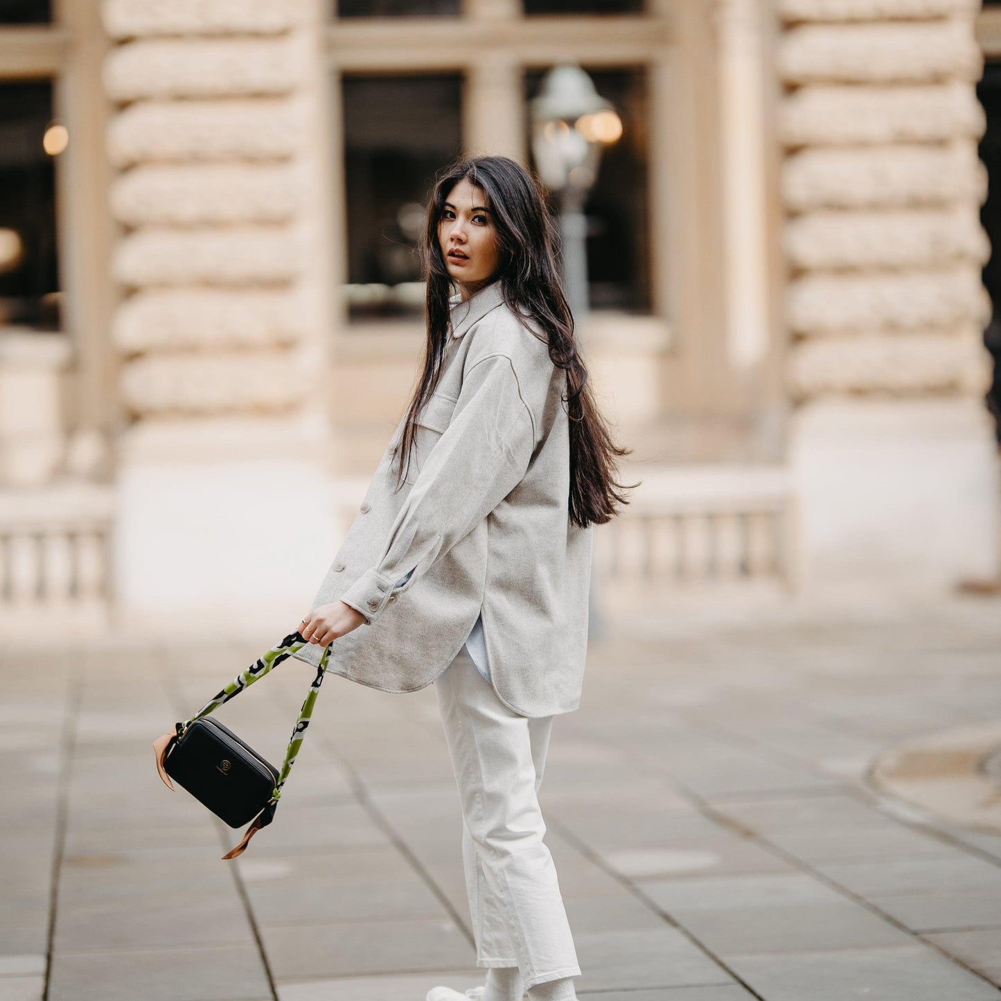 Eine junge Frau dreht sich mit Schwung um und die Jade in schwarz mit dem Analou Leopard Twill Schal als Taschengurt trägt sie in der Hand