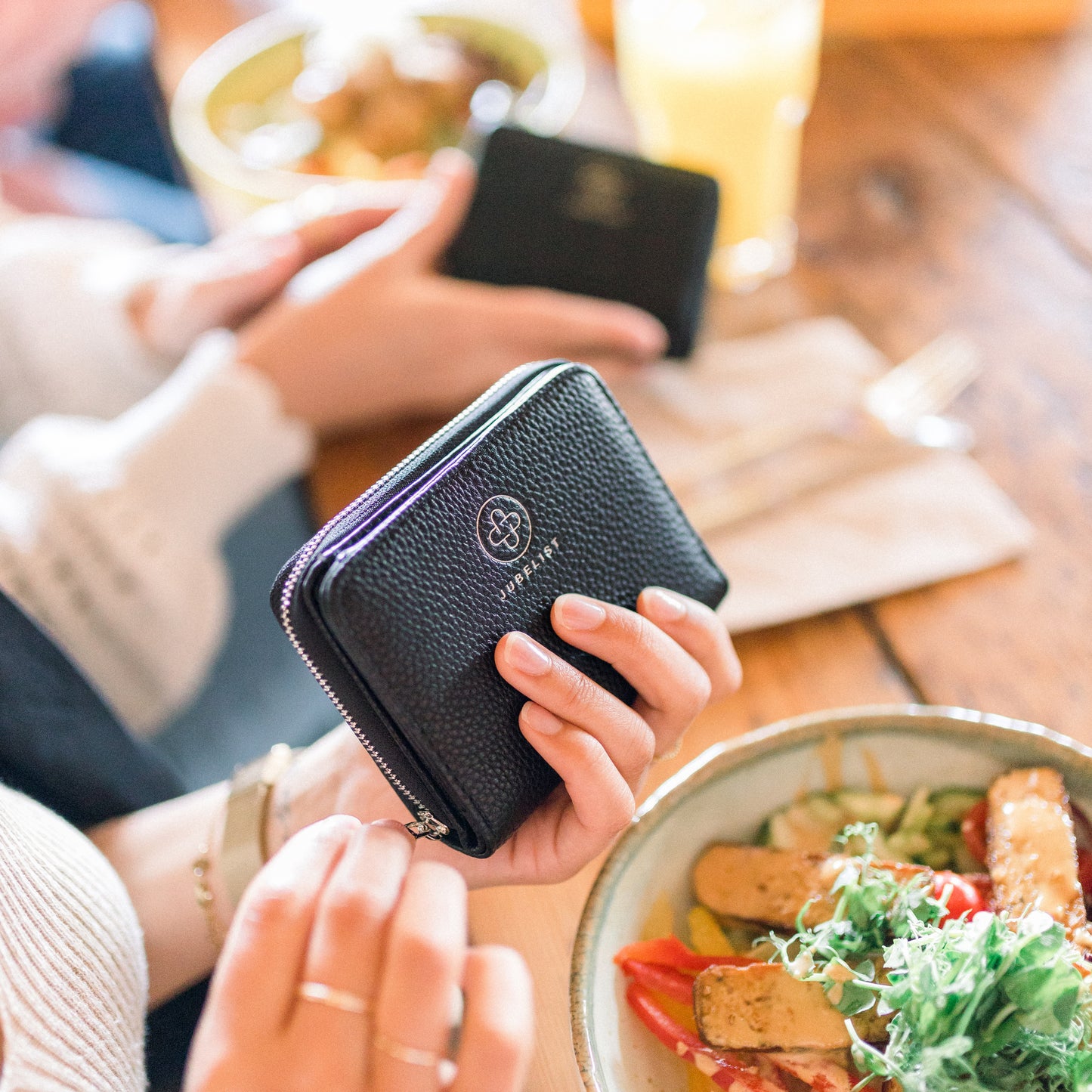 Das Portemonnaie in schwarz-silber wird in einer Hand gehalten und mit der anderen Hand wird der Reißverschluss geöffnet