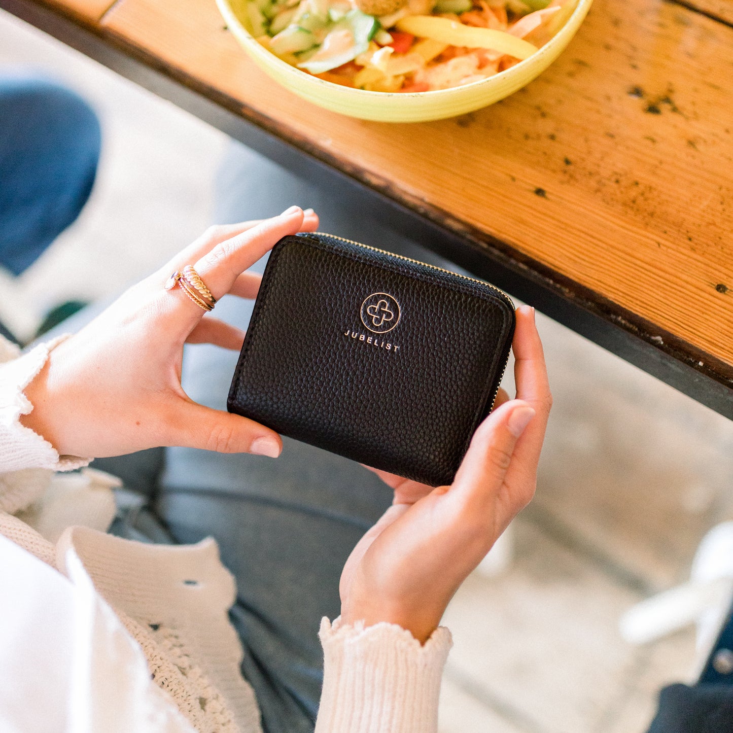 Das schwarze Medium Size wird in beiden Händen gehalten, man erkennt das genarbte Material und das Jubelist Logo