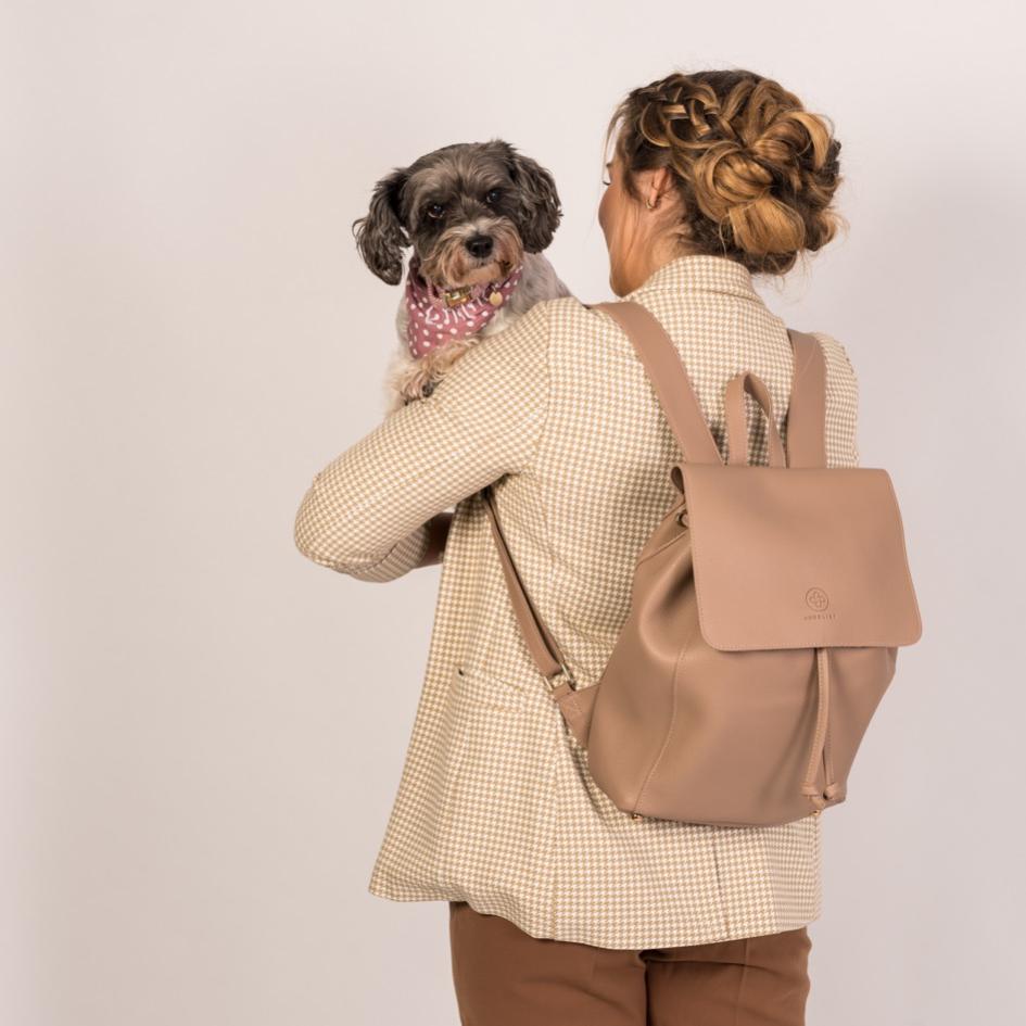 Eine Frau in einer gemusterten Jacke trägt den Rucksack KATE, die hat eine Hund auf dem Arm, der über ihre Schulter schaut.