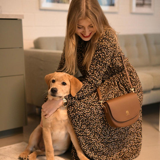 Anna kniet bei einem Labrador Welpen und trägt ihre Tasche in coffee crossbody