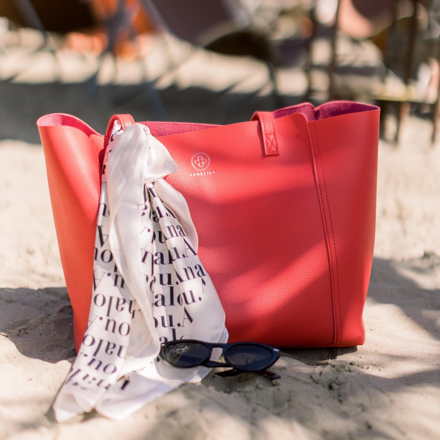 Die Victoria in rot steht im Sand und das Analou Logo Chiffontuch ist als Accessoire an einem Tragegurt befestigt