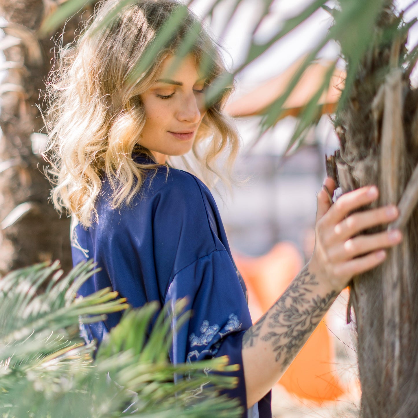 Influencerin Anna steht verträumt unter Palmen in einem saphierblauen Kimono