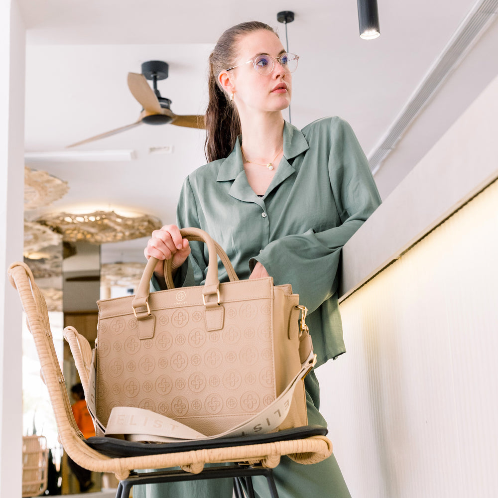 
                  
                    Die taupe farbende Business Bag steht auf einem Barhocker im Fokus.
                  
                