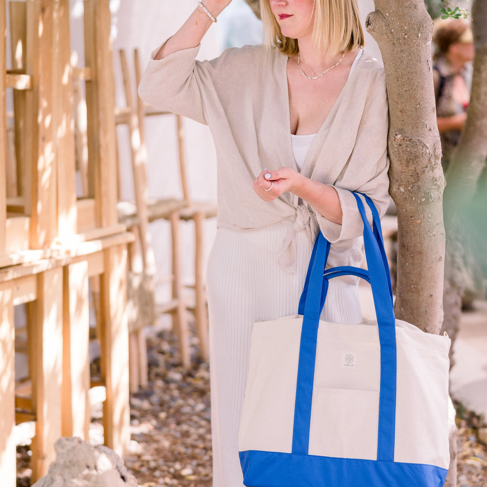 
                  
                    Tina Ruthe steht an einem Baum gelehnt mit der blauen Canvas Bag in der Hand.
                  
                