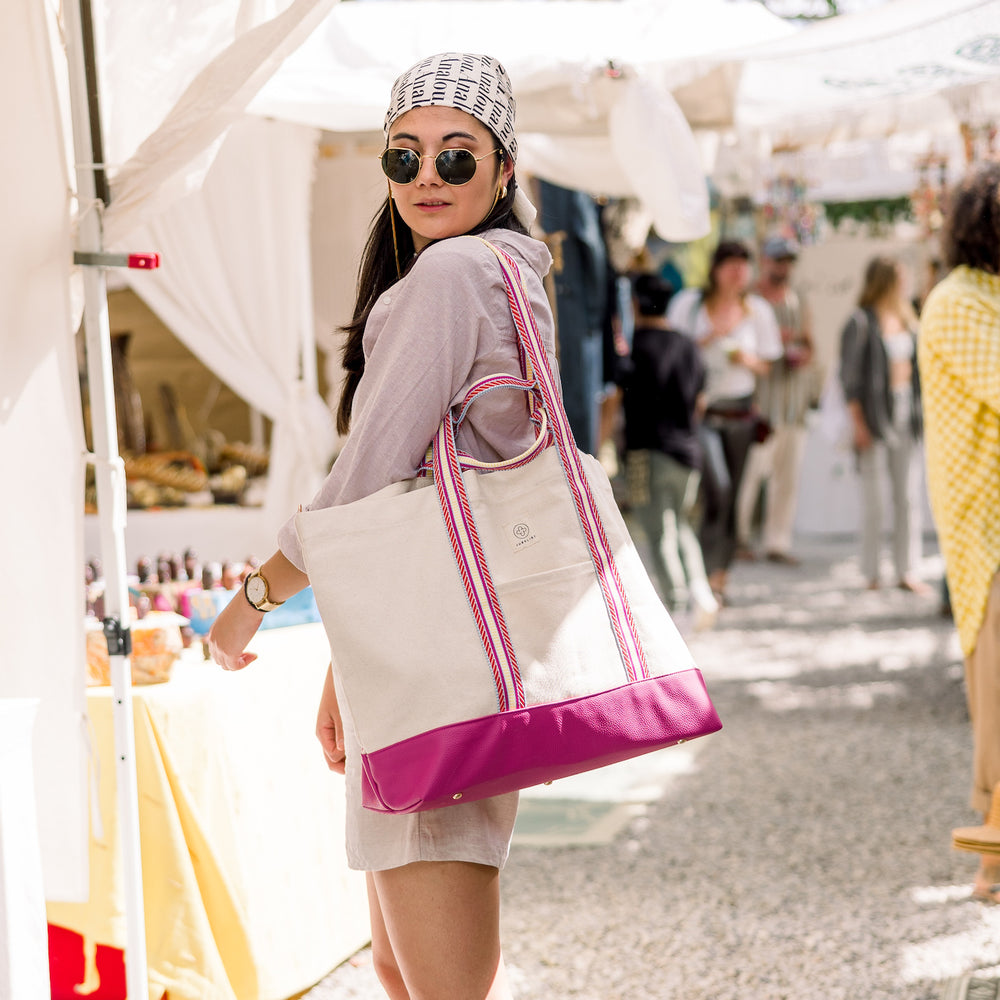 
                  
                    Vorm Hippie-Markt in Ibiza steht das Model mit der pinken Canvas Bag mit gestreiften Henkeln.
                  
                