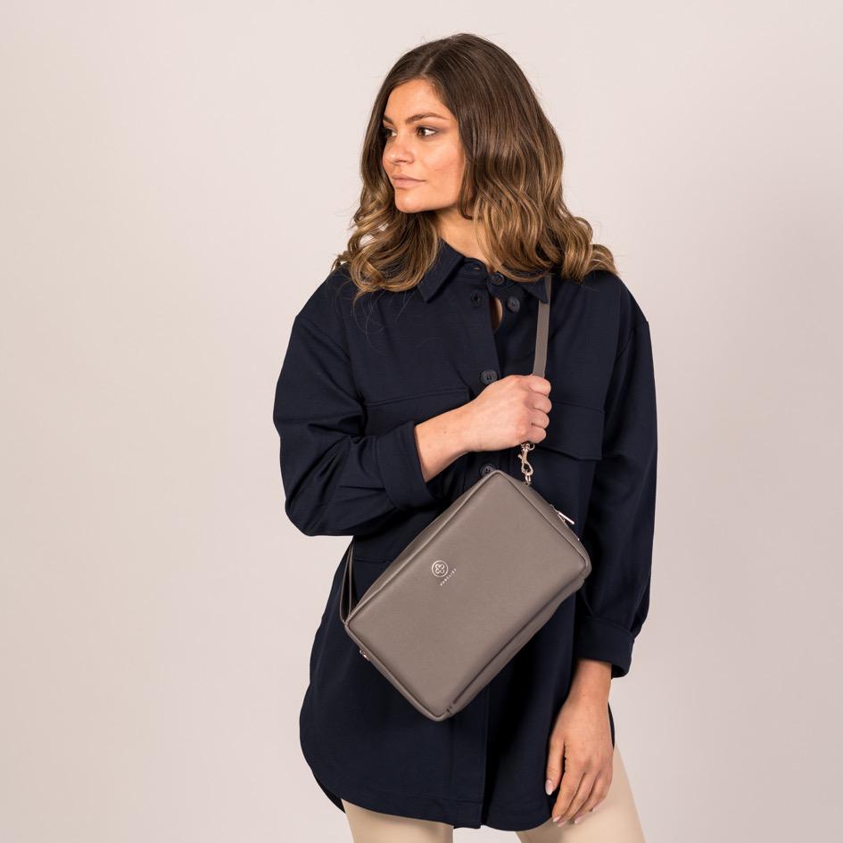 
                  
                    Ein Model trägt die ZOE XL in graphite / silber crossbody vor dem Bauch
                  
                