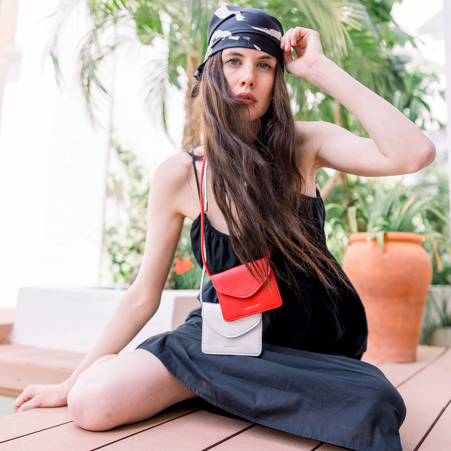 Ein Model trägt das rote und silberne Portemonnaie BAILY um den Hals, sie trägt ein schwarzes Kleid und ihre dunkelbraunen Haare wehen im Wind.
