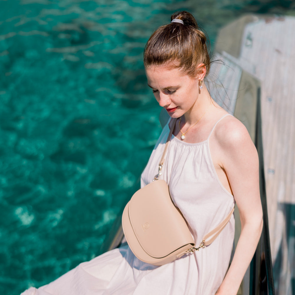 
                  
                    Ein Model sitzt in einem weißen Kleid am Bug eines Bootes und trägt die sandfarbene Saddle Bag.
                  
                