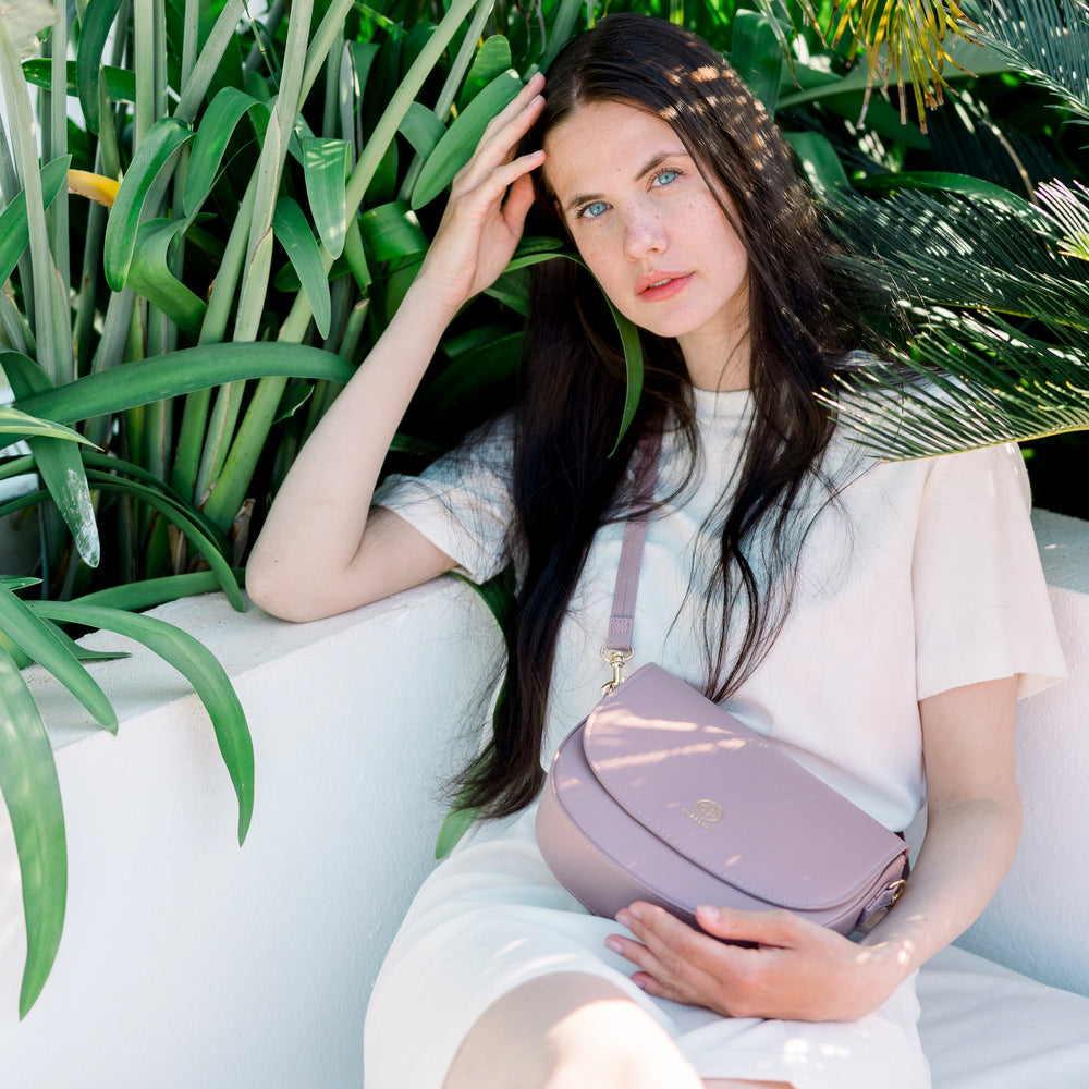 
                  
                    Ein Model mit blauen Augen und schwarzem Haar trägt die Saddle Bag in puder.
                  
                