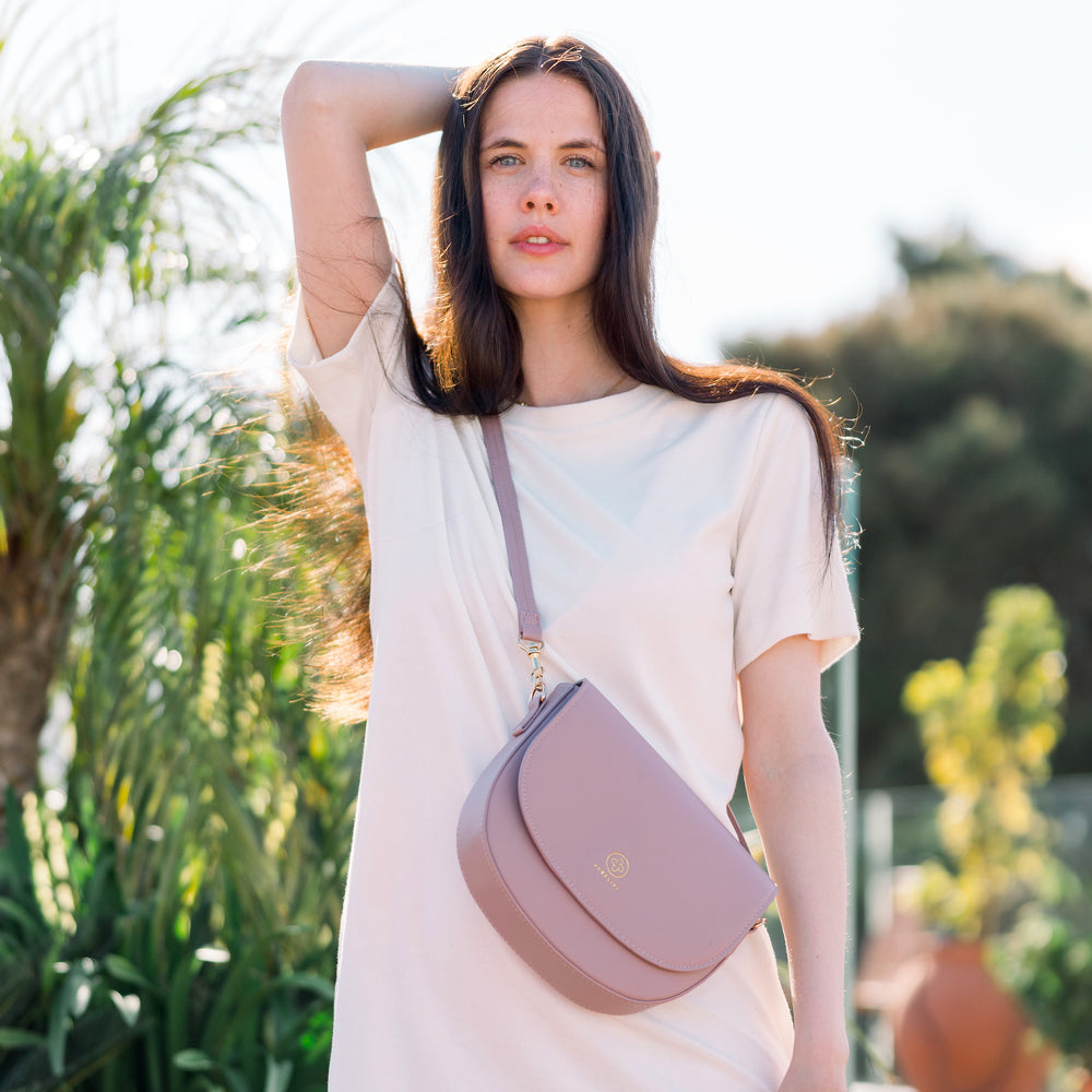 
                  
                    Ein Model mit dunklen Haar schaut direkt in die Kamera, einen Arm über den Kopf gestreckt, während sie die Saddle Bag in puder trägt.
                  
                