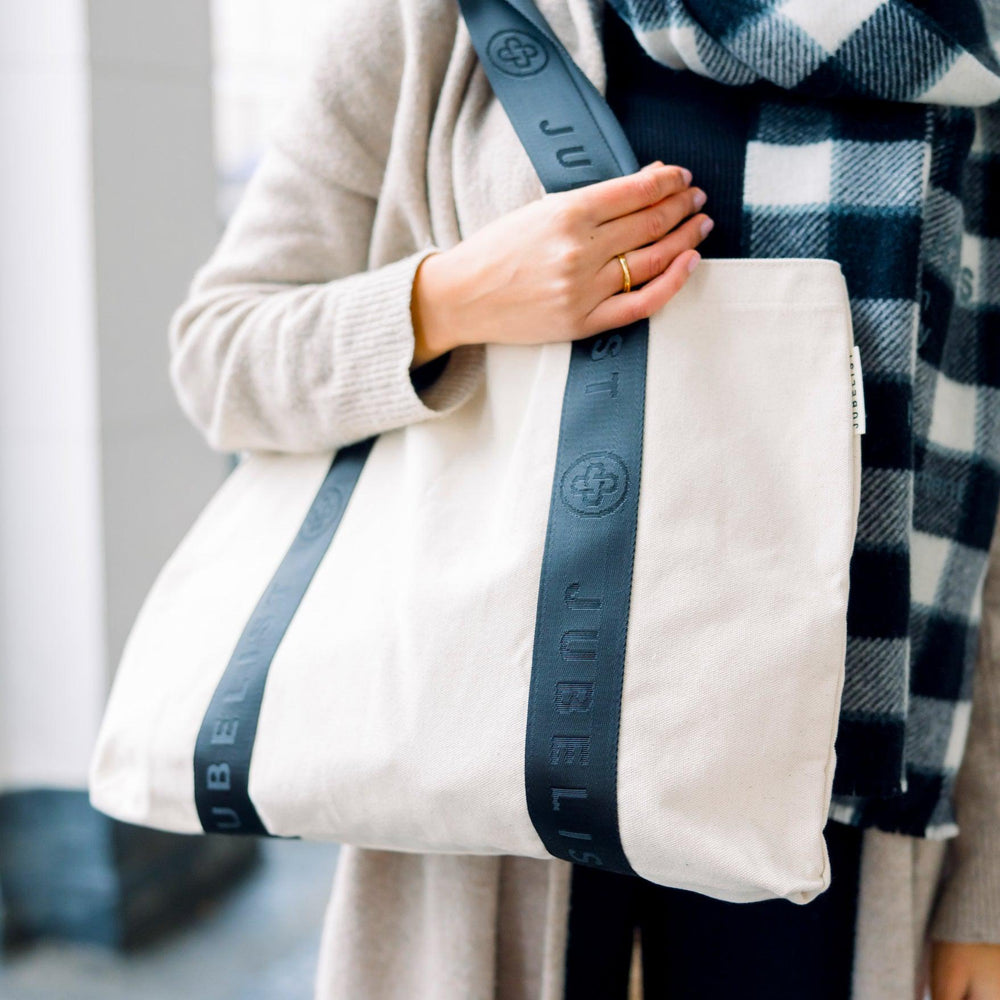 
                  
                    Eine Nahaufnahme des Canvas Shopper mit schwarzen Griffen zeigt das tolle Jubelist Logo auf dem Gurt
                  
                