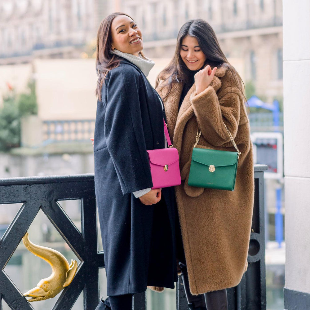 
                  
                    zwei junge Frauen stehen beieinander, die eine trägt die Tasche in hot pink crossbody und die andere hat die grüne Tasche mit der Kette als Taschengurt über ihrem Unterarm
                  
                