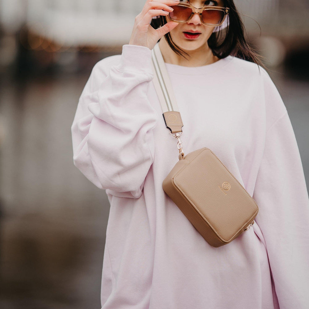 
                  
                    Die Jade in taupe wird mit dem Universal Strap in beige weiß crossbody getragen
                  
                