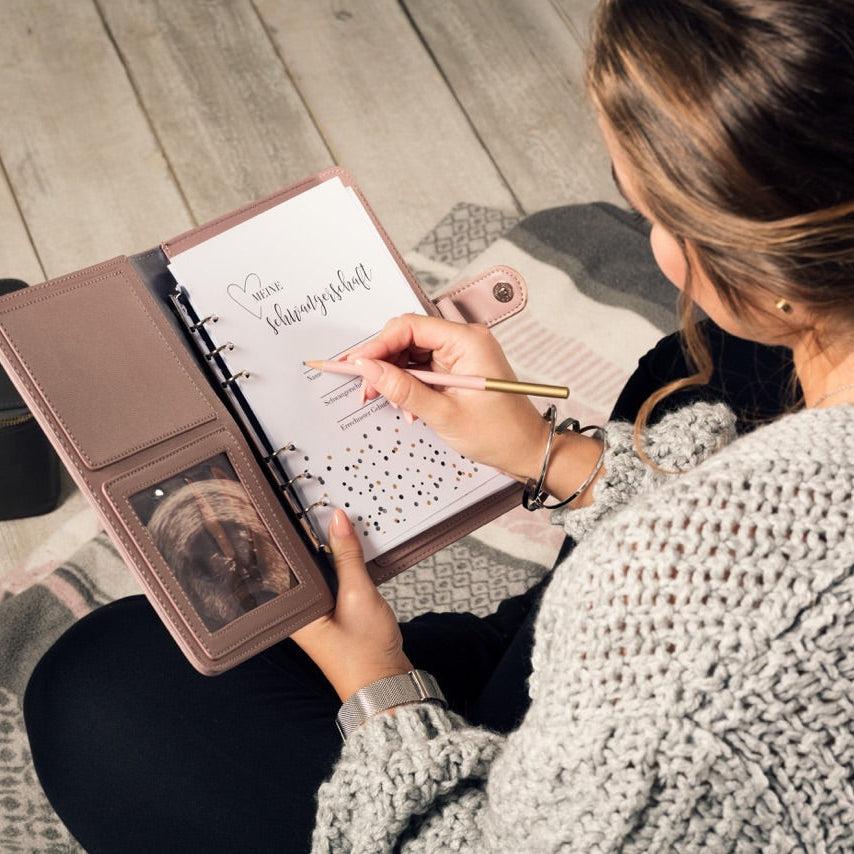 Eine junge Frau hat den Organizer in puder aufgeklappt vor sich und schreibt ihren Namen in das Buch