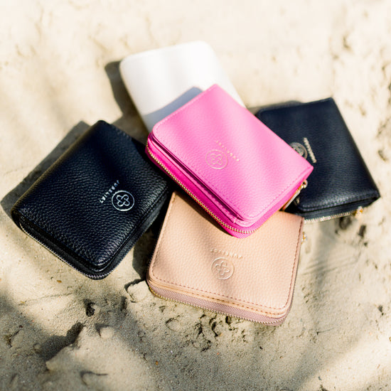 Die Portemonnaies liegen aufeinander gestapelt im Sand, hot pink im Fokus