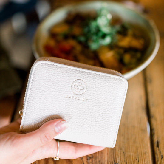 In einem Restaurant wird das weiße Portemonnaie in einer Hand gehalten und man erkennt das eingeprägte Logo im genarbten Material