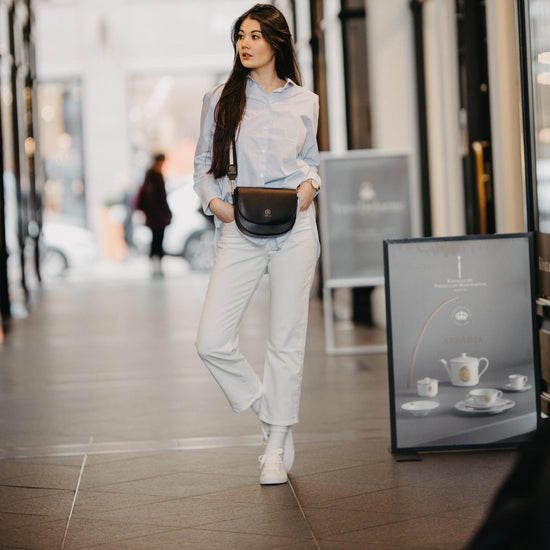 Eine junge Frau schlendert mit ihrer Tasche kombiniert mit dem Universal Strap in schwarz weiß durch eine Einkaufspassage