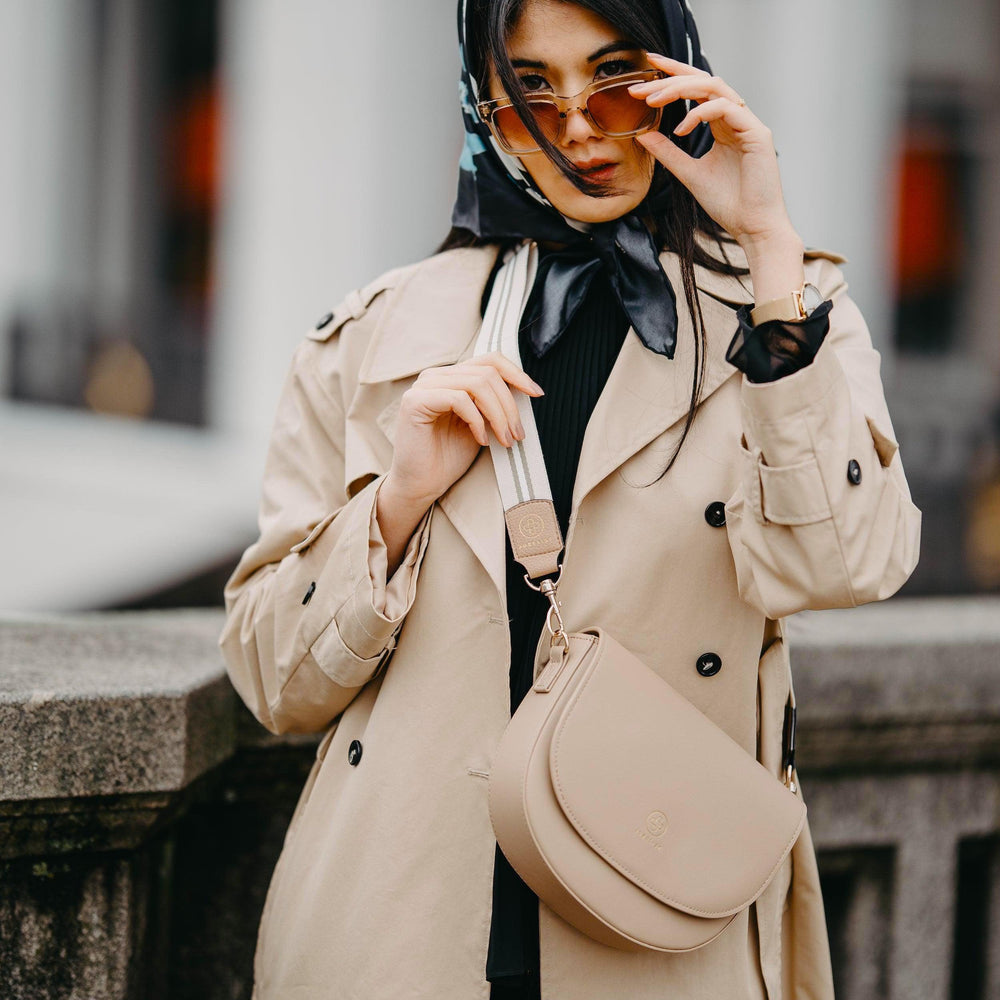 
                  
                    Eine junge Frau trägt die Saddle Bag in sand kombiniert mit dem Universal Strap in beige weiß crossbody
                  
                