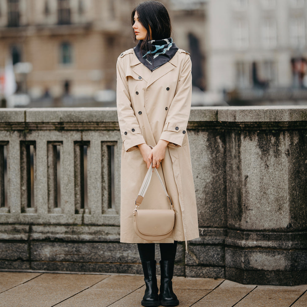 
                  
                    Die Saddle Bag in sand kombiniert mit dem Universal Strap in beige weiß wird von einer jungen Frau in den Händen gehalten
                  
                