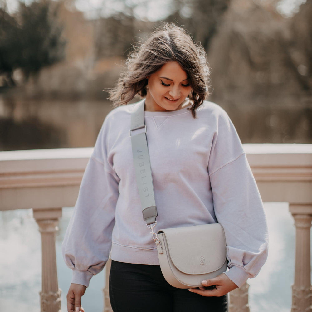 
                  
                    Eine junge Frau trägt eine Saddle Bag in stone kombiniert mit einem Fashion Strap in graphite silber
                  
                