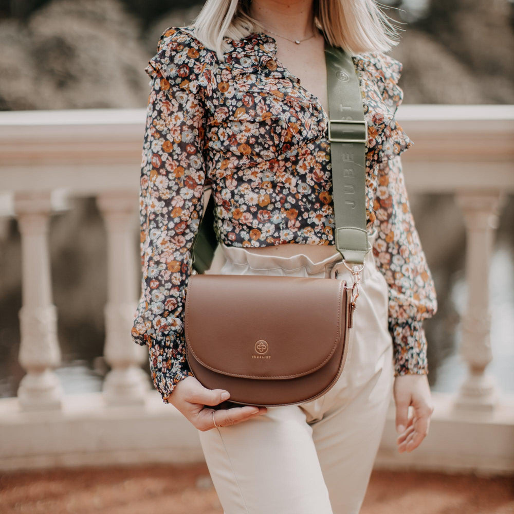 
                  
                    Eine Nahaufnahme zeigt die Saddle Bag in coffee mit dem Fashion Strap in khaki
                  
                
