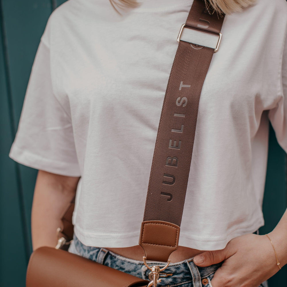 
                  
                    Diese Nahaufnahme zeigt den Fashion Strap in coffee mit dem Schriftzug Jubelist
                  
                