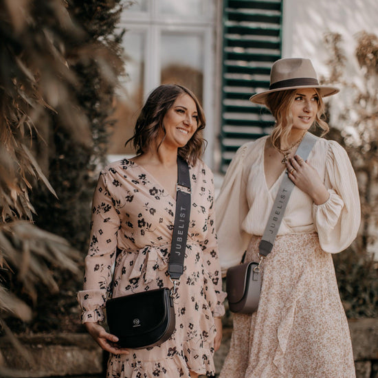 Zwei junge Frauen stehen nebeneinander in sommerlichen Kleidern und jede trägt eine Saddle Bag mit einem Fashion Strap
