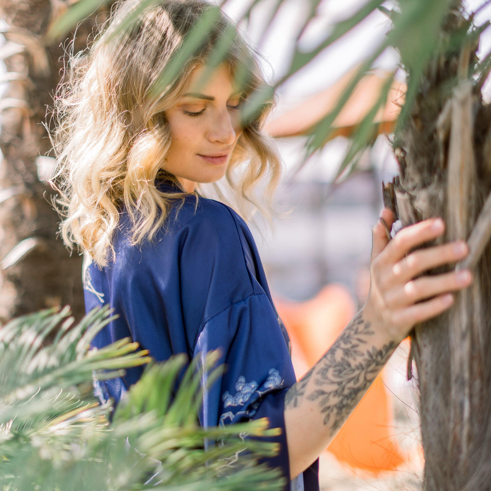 
                  
                    Influencerin Anna steht verträumt unter Palmen in einem saphierblauen Kimono
                  
                